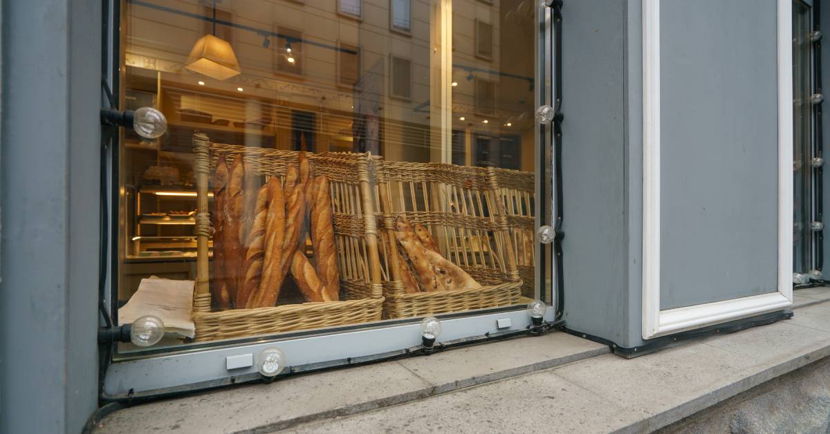 An outdoor look into a bakery. There are baguettes sitting in baskets displayed in the bakery window.