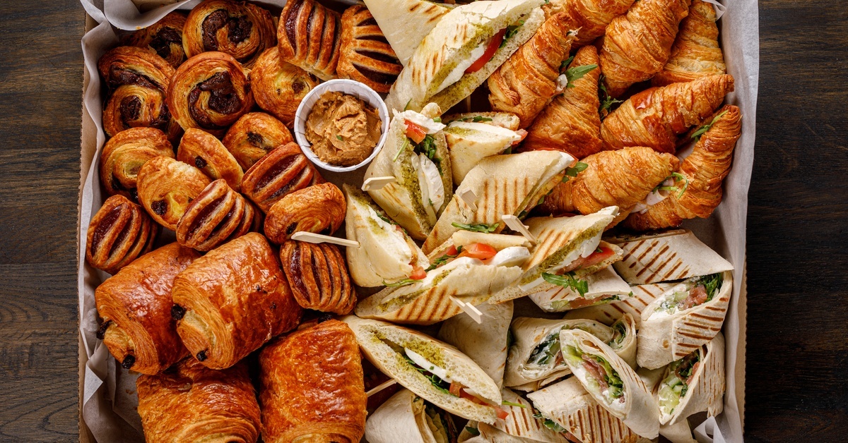 Dos and Don’ts When Sourcing Catering Boxes An aerial view shows a brown catering box filled with various pastries and sandwiches, along with a small cup of red dip.