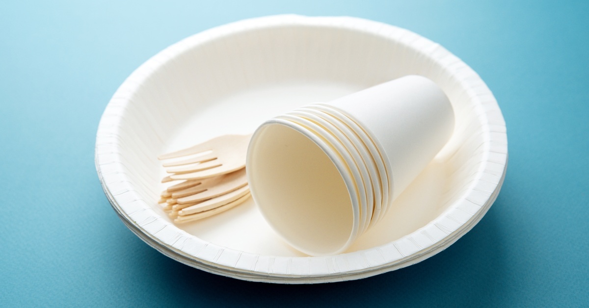 Pros and Cons of Disposable vs. Reusable Plates A small stack of disposable plates with a few stacked disposable cups and forks on top of the plates.