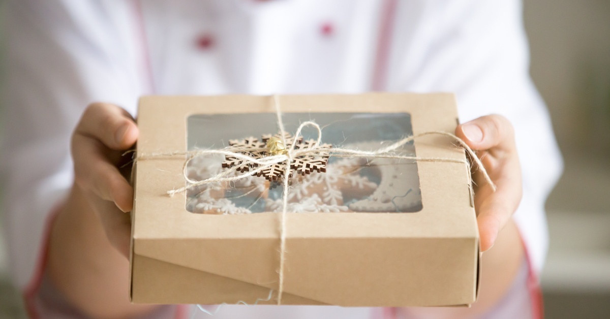 A baker in a white jacket holds a kraft paper bakery box tied with twine and decorated with a wooden snowflake ornament. A baker in a white jacket holds a kraft paper bakery box tied with twine and decorated with a wooden snowflake ornament.