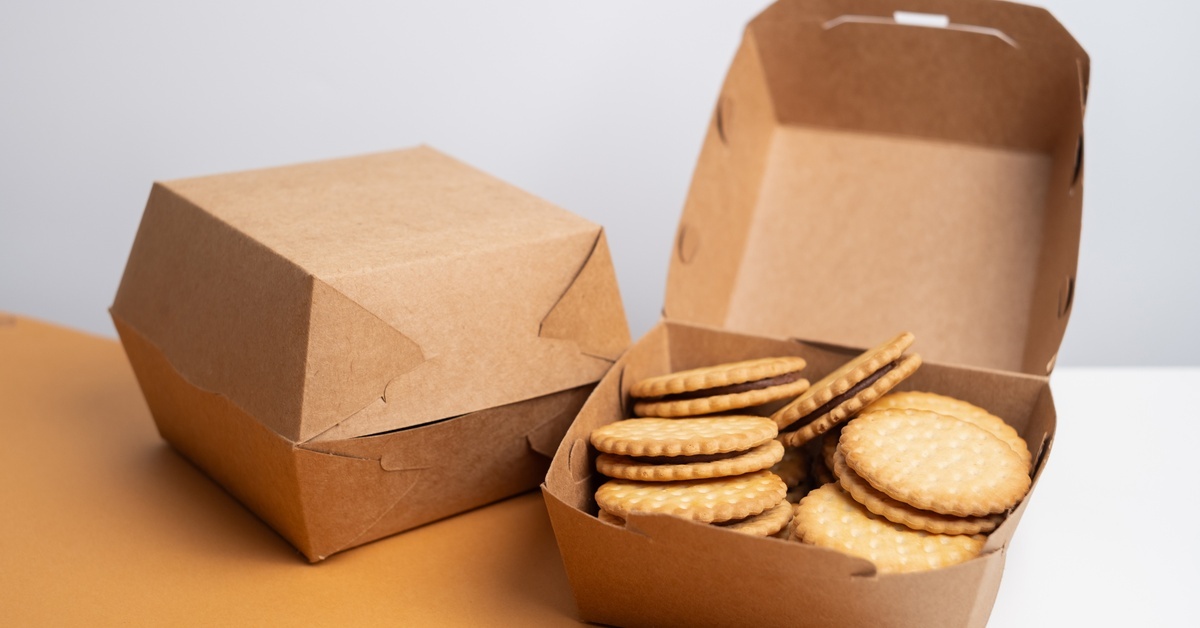 Two small cardboard containers on a brown table. One container is open, revealing small cookies inside.