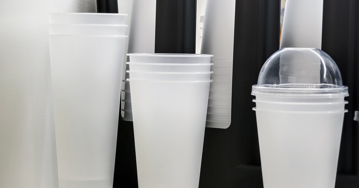 Stacked clear plastic cups with lids are displayed on a shelf, showing different sizes for cold drinks and smoothies.