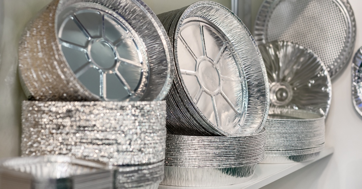 Stacks of round and rectangular aluminum foil pans displayed on a shelf in a foodservice supply area. Stacks of round and rectangular aluminum foil pans displayed on a shelf in a foodservice supply area.