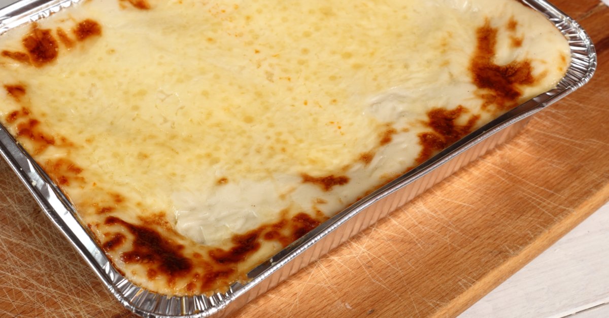 The Advantages of Aluminum Foil for Oven-Ready Meals A freshly baked lasagna with a golden-browned cheese topping in an aluminum foil tray resting on a wooden cutting board.