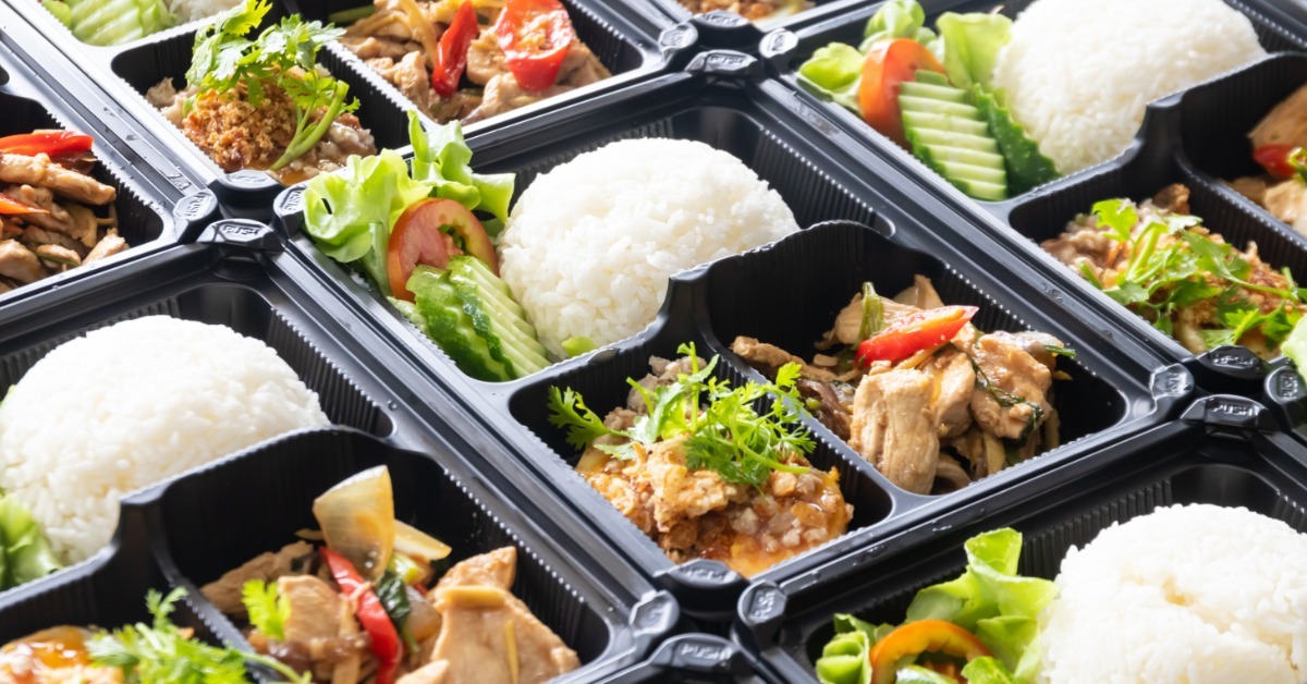 Many black bento-style catering boxes with rice, chicken stir-fry, and colorful vegetable sides.