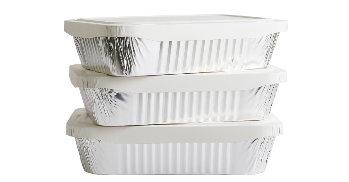 A close-up of three identical rectangular aluminum food containers with white lids stacked on top of one another.