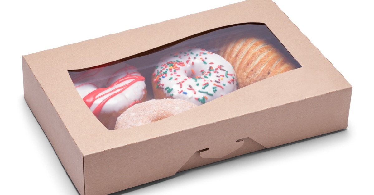 A brown bakery box with a plastic window showing multiple doughnuts inside, including frosted and sugar pastries.