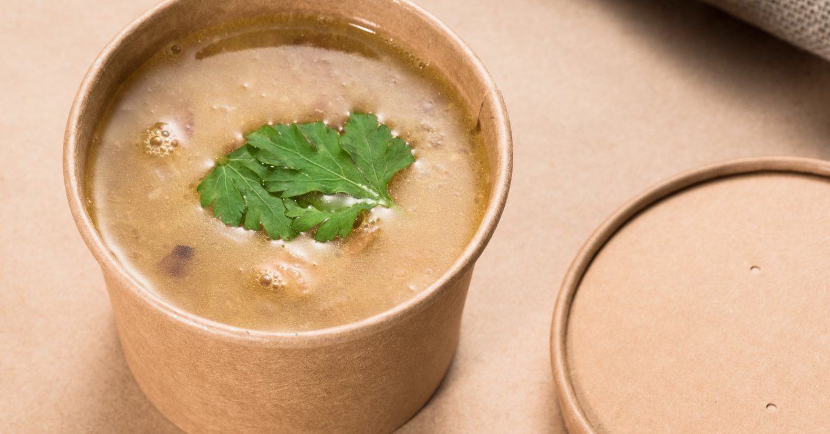 How To Choose the Right Soup Container Lid A close-up of a soup with leaves as a garnish in a brown, disposable paper container with the lid next to it.