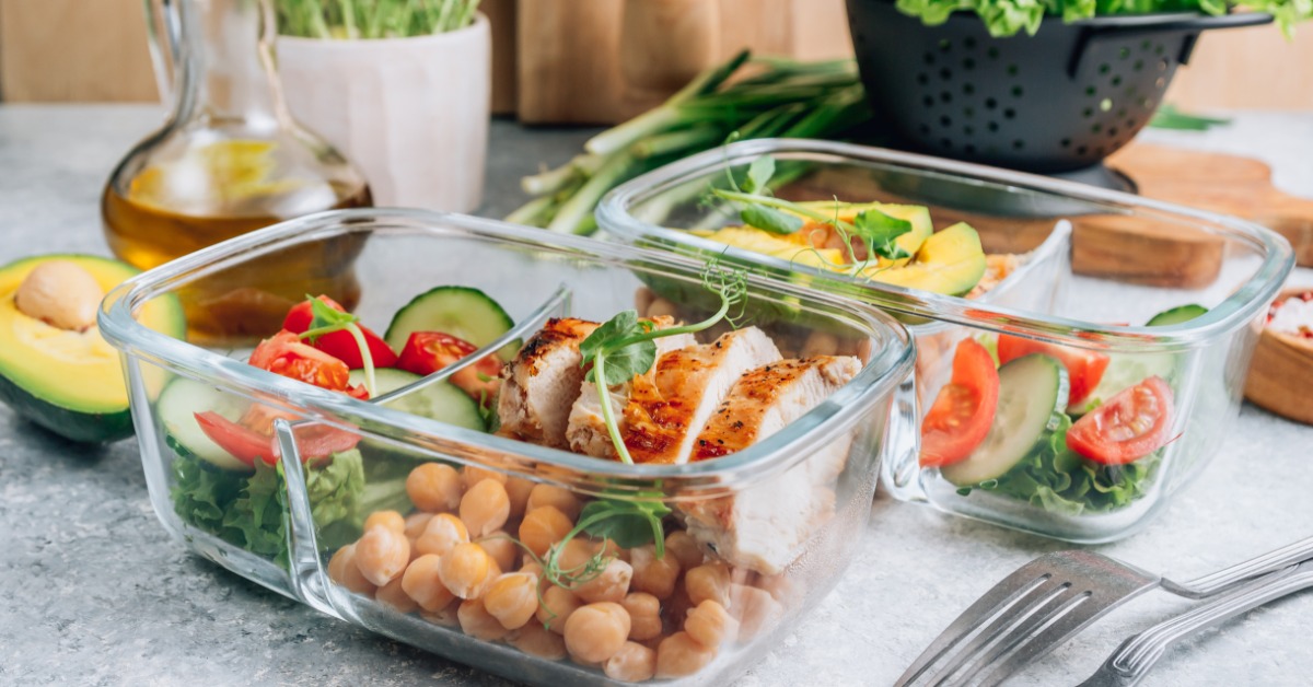 A close-up of two glass compartment meal prep containers containing grilled chicken, chickpeas, and vegetables.