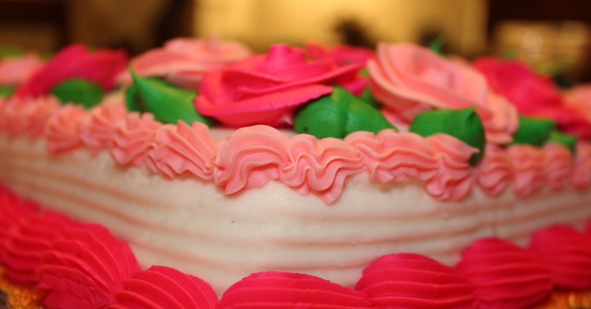 A close-up of the corner of a white sheet cake on a platter decorated with red, pink, and green frosting.