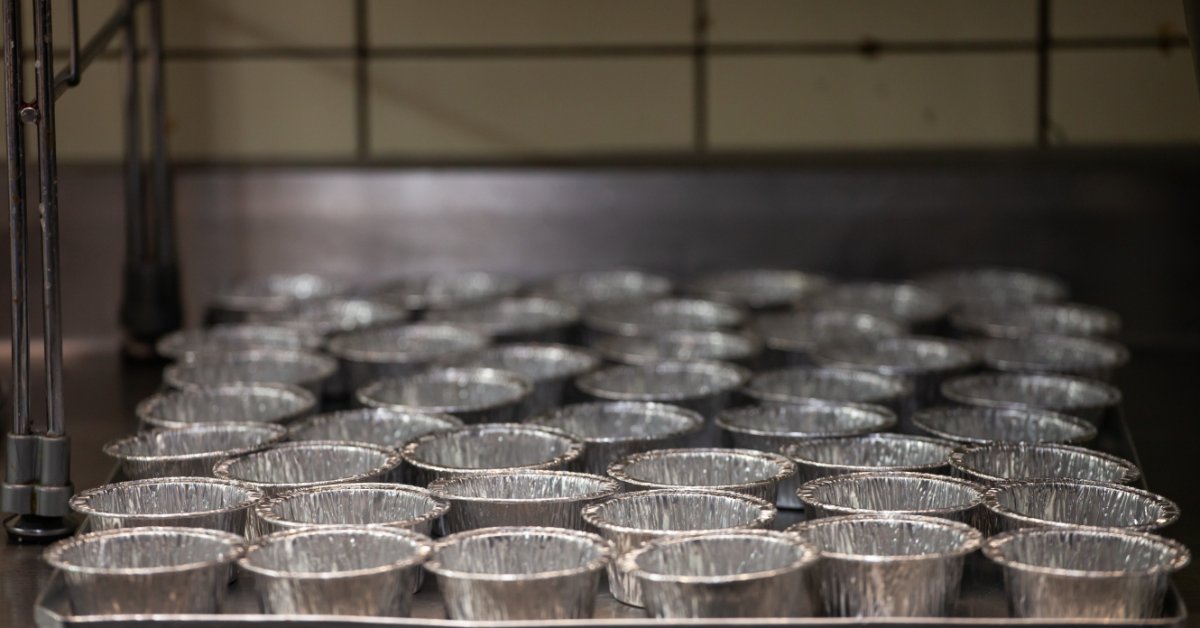 A side-view close-up of a large baking sheet on a cooling rack filled with small, round aluminum foil pans.