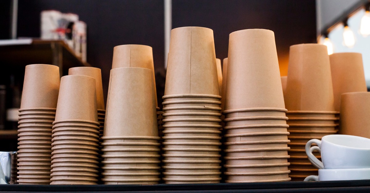 Multiple stacks of disposable coffee cups made from a recycled brown paper material on a black tabletop.