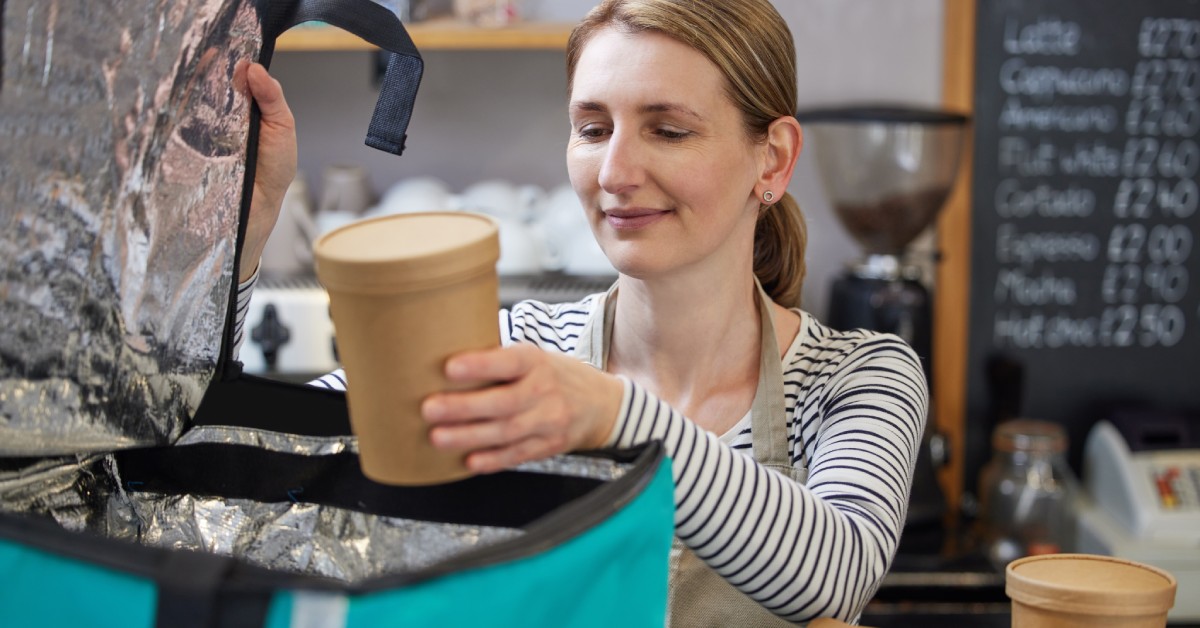 A restaurant worker loading up an insulated bag with several brown paper food packages for delivery.