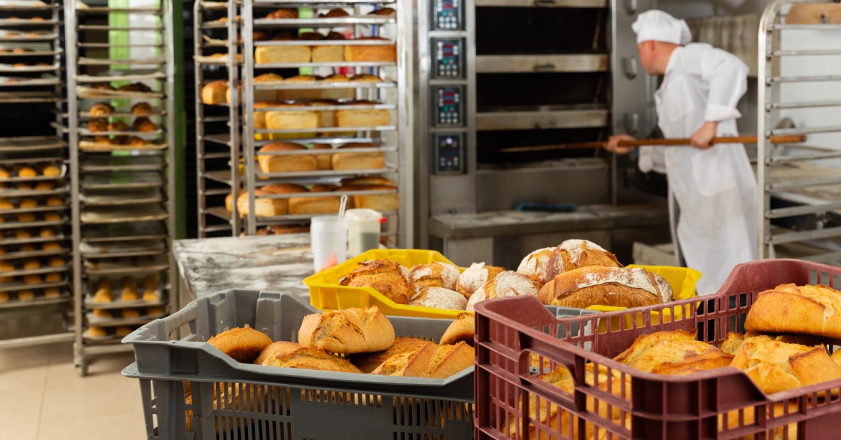 Three boxes with fresh bread in a bakery as a baker in a traditional hat gets more baked goods out of the oven.