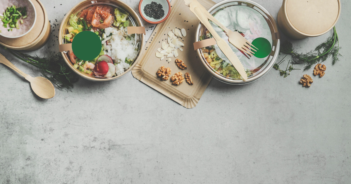 Wooden recyclable cutlery, including forks, spoons, and knives, in a brown paper coffee cup on a green background.