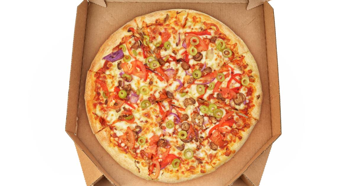 An open brown cardboard pizza box with a pizza inside covered in jalapenos, tomatoes, and onions.