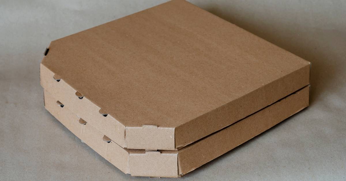 A simple stack of two brown cardboard pizza boxes made of corrugated material on a plain gray background.