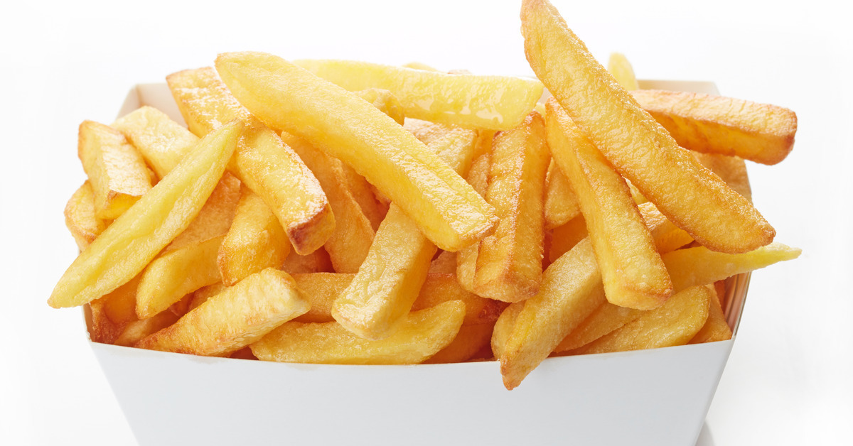 A small white cardboard container full of classic French fries which have light salt and seasoning on a plain background.