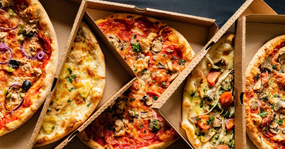 Five different types of pizzas with various toppings in cardboard pizza boxes against a dark gray background.