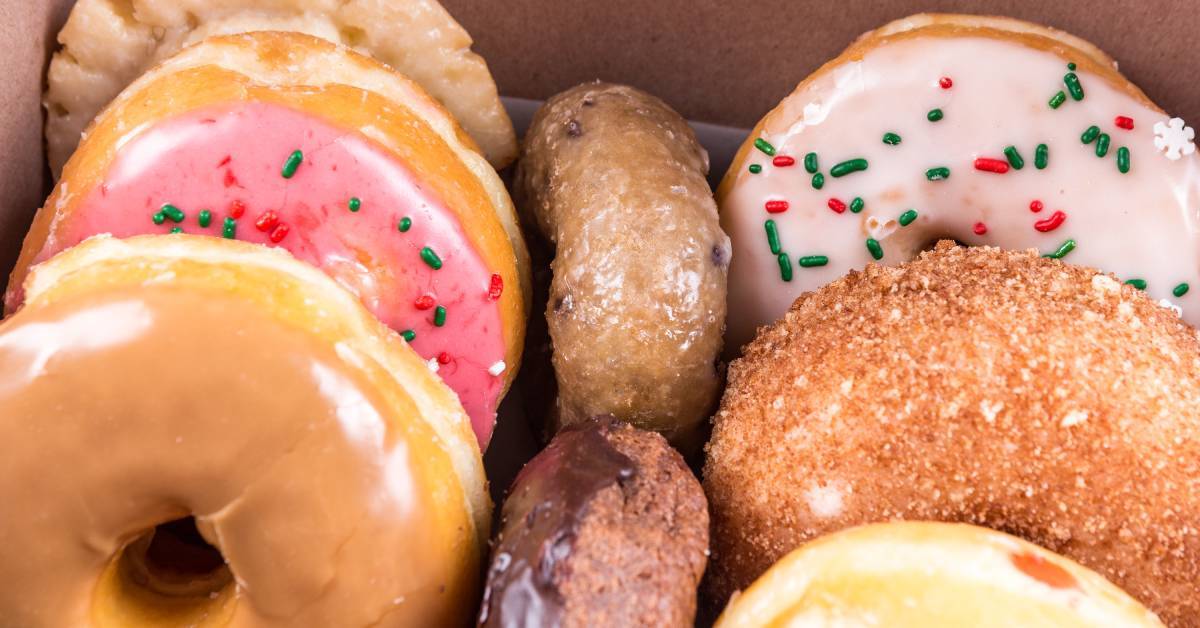 A box of colorful assorted donuts with glazed, sprinkled, chocolate, sugar-covered, and frosted options.