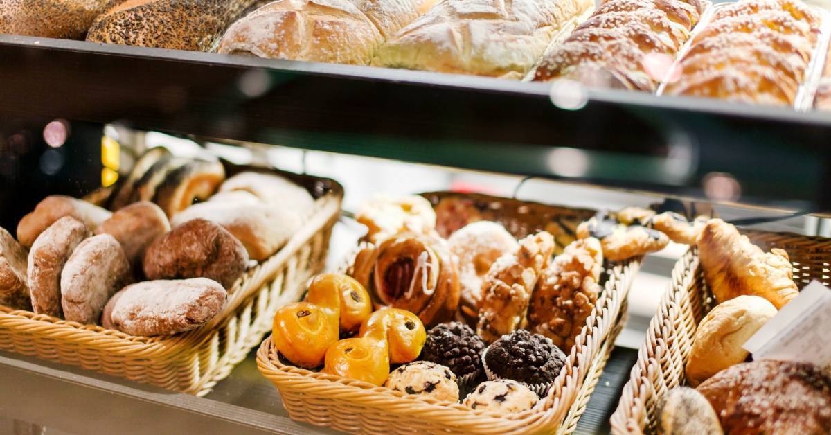 Several baked goods, including bread, muffins, and other pastries, in baskets arranged at a bakery counter.