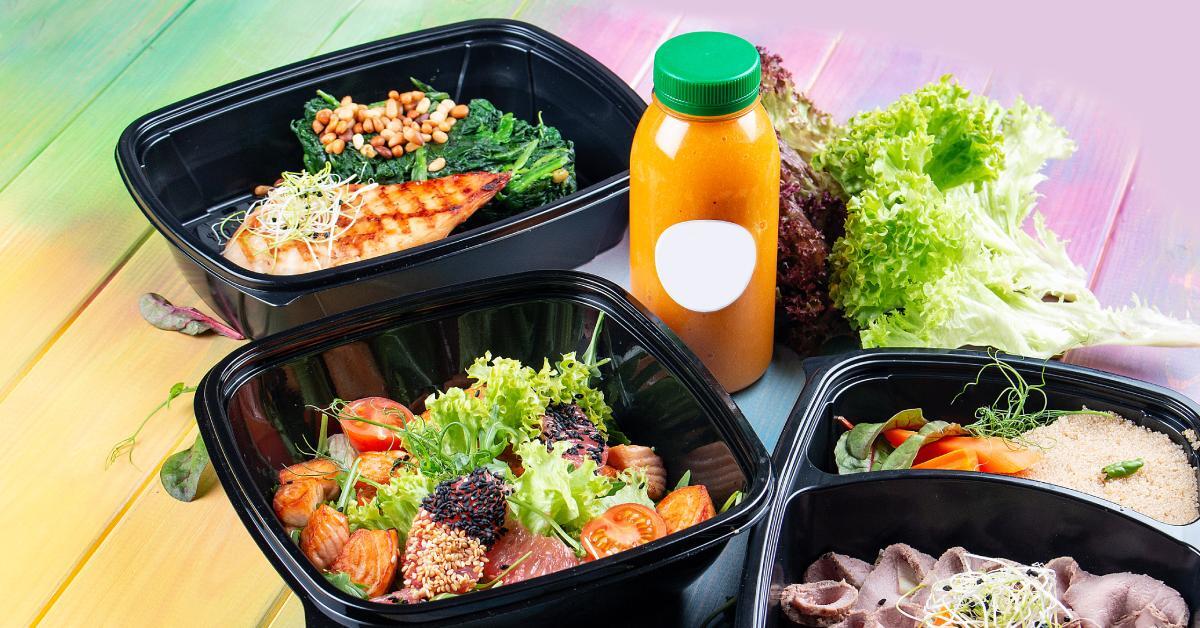 A set of fine dining dishes with vegetables and nice plating in plastic takeout containers on a simple wooden table.