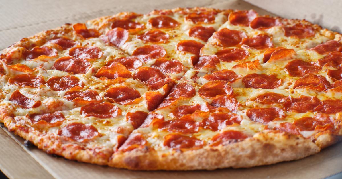 A close-up on a large cheese and pepperoni pizza with a shine of grease on top resting in a cardboard pizza box.