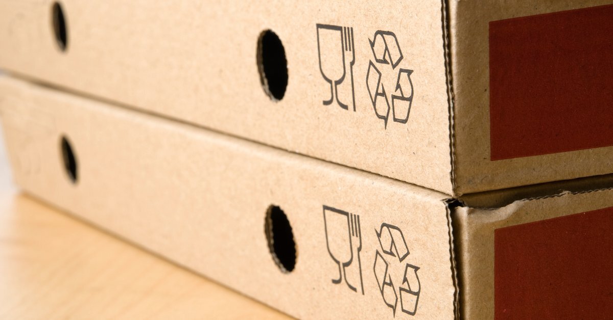 A close-up of two cardboard pizza boxes sitting on top of each other. Both boxes feature the recycling symbol.