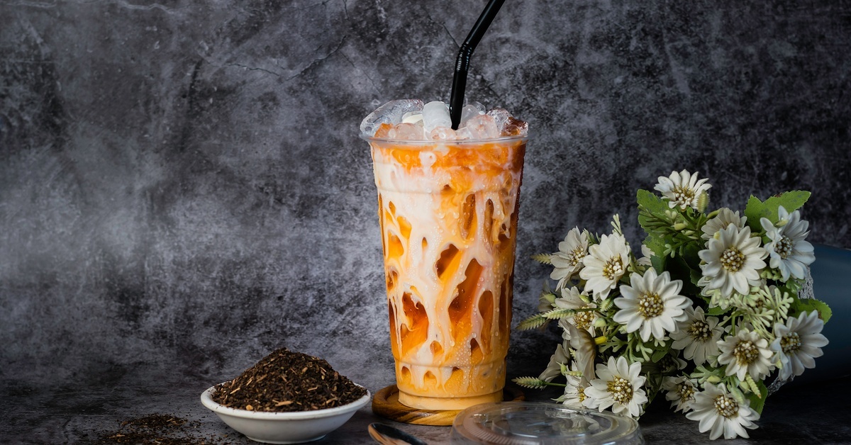 A heaping cup of red tea sits in a plastic cup, with a black straw protruding from it. Flowers sit next to it. A heaping cup of red tea sits in a plastic cup, with a black straw protruding from it. Flowers sit next to it.