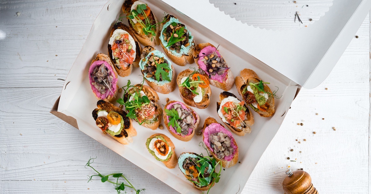 Overhead view of a cardboard box featuring canapés inside. The box sits on a white counter next to a spice grinder. Overhead view of a cardboard box featuring canapés inside. The box sits on a white counter next to a spice grinder.