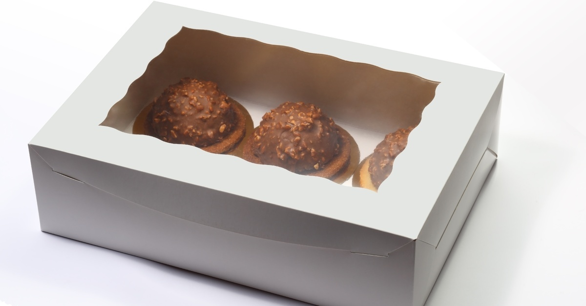 Three small chocolate cakes sit inside a plain white box. It features a clear window that gives a view of them.