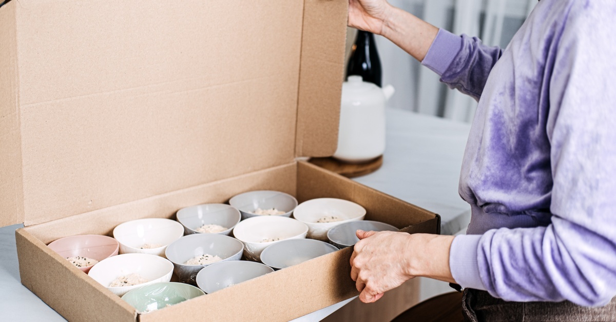 A person in a purple sweatshirt opens a large catering box, which features several small bowls of oatmeal.
